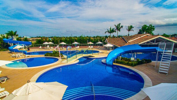 Una gran piscina exterior con varias pistas de natación, rodeada de sillas de descanso y sombrillas.