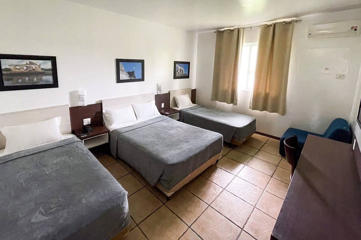 A hotel room with two single beds, a desk, a chair, and a window with curtains.