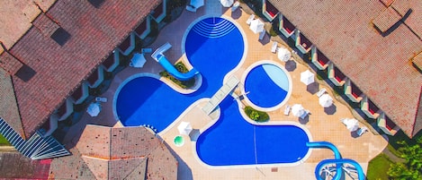 An aerial view of a resort with multiple swimming pools, sun loungers, umbrellas, and a water slide.