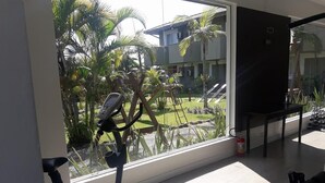 Habitación con un ventanal grande, una caminadora y vistas a un patio con palmeras y un edificio al fondo.