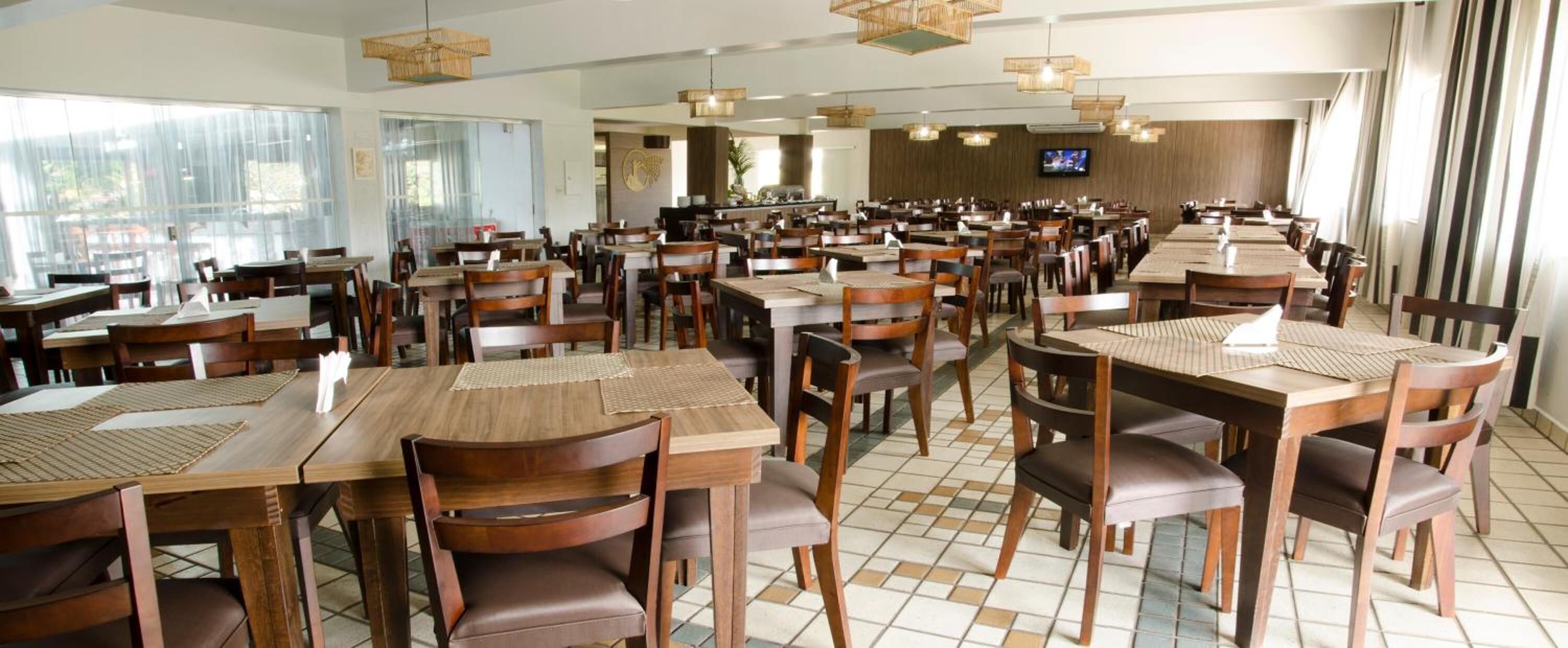 En rummelig restaurant med flere træborde og stole, store vinduer og hængende lamper.