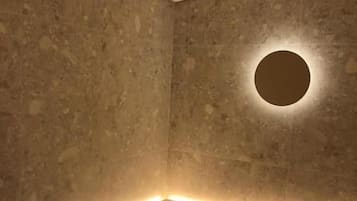 Canto de um quarto com luminária circular na parede e fita de luz ao longo do rodapé.