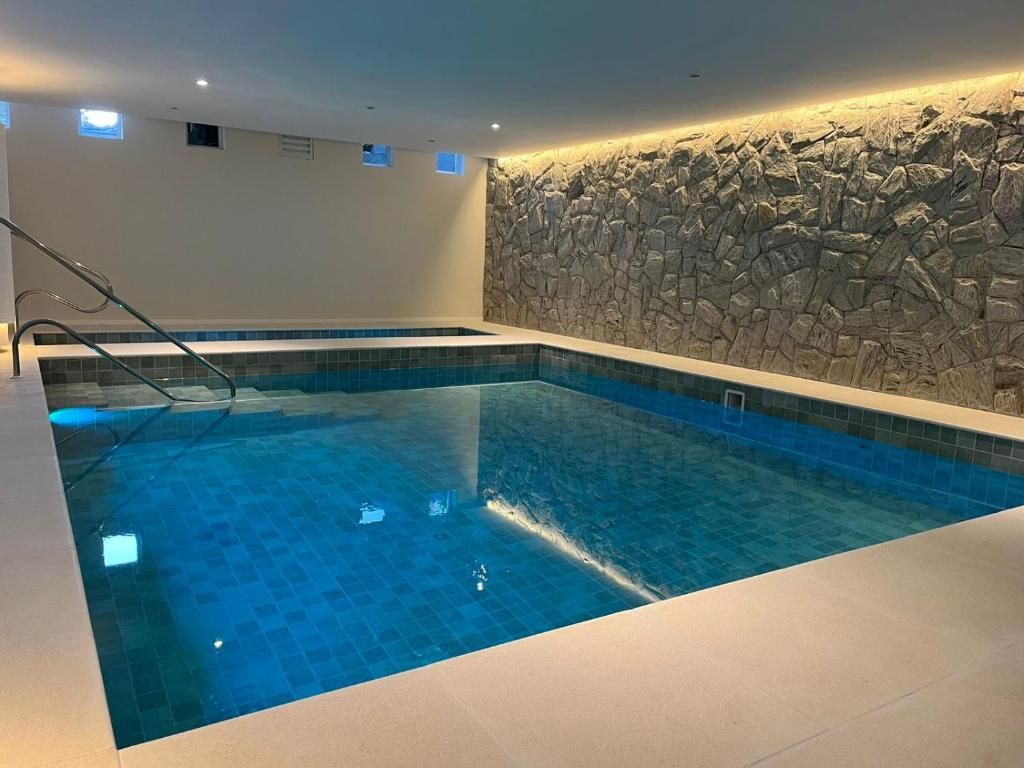 A swimming pool with a stone wall backdrop and a clear blue tiled floor.