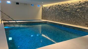 A swimming pool with a stone wall backdrop and a clear blue tiled floor.