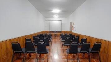 A conference room with rows of black chairs, a whiteboard, and a tiled floor.