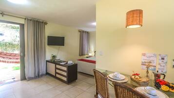 Quarto de hotel com cama, escrivaninha, televisão, área de refeições com mesa e cadeiras, e vista para o exterior.