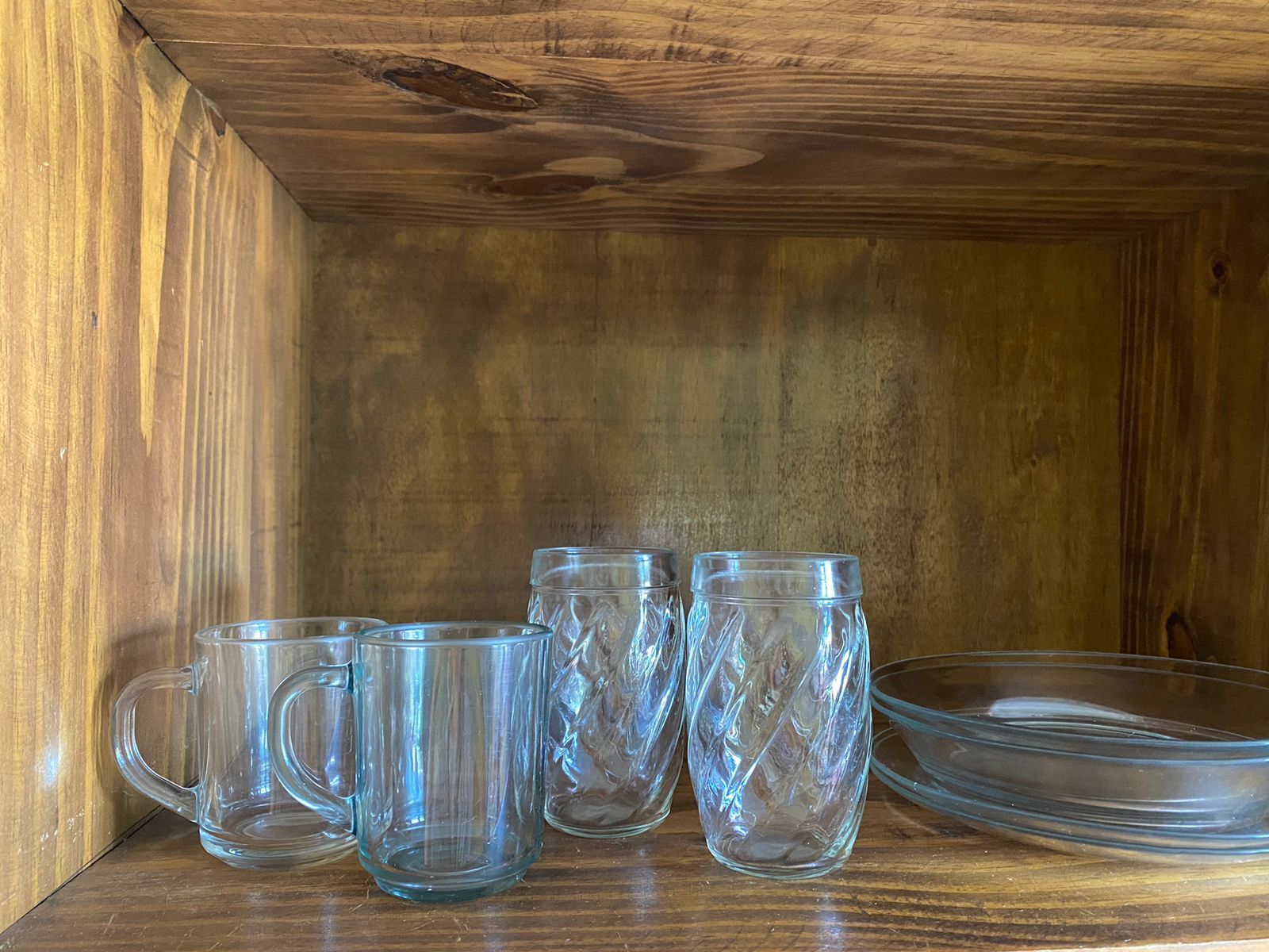A wooden cabinet with four clear glass mugs and a clear glass bowl.