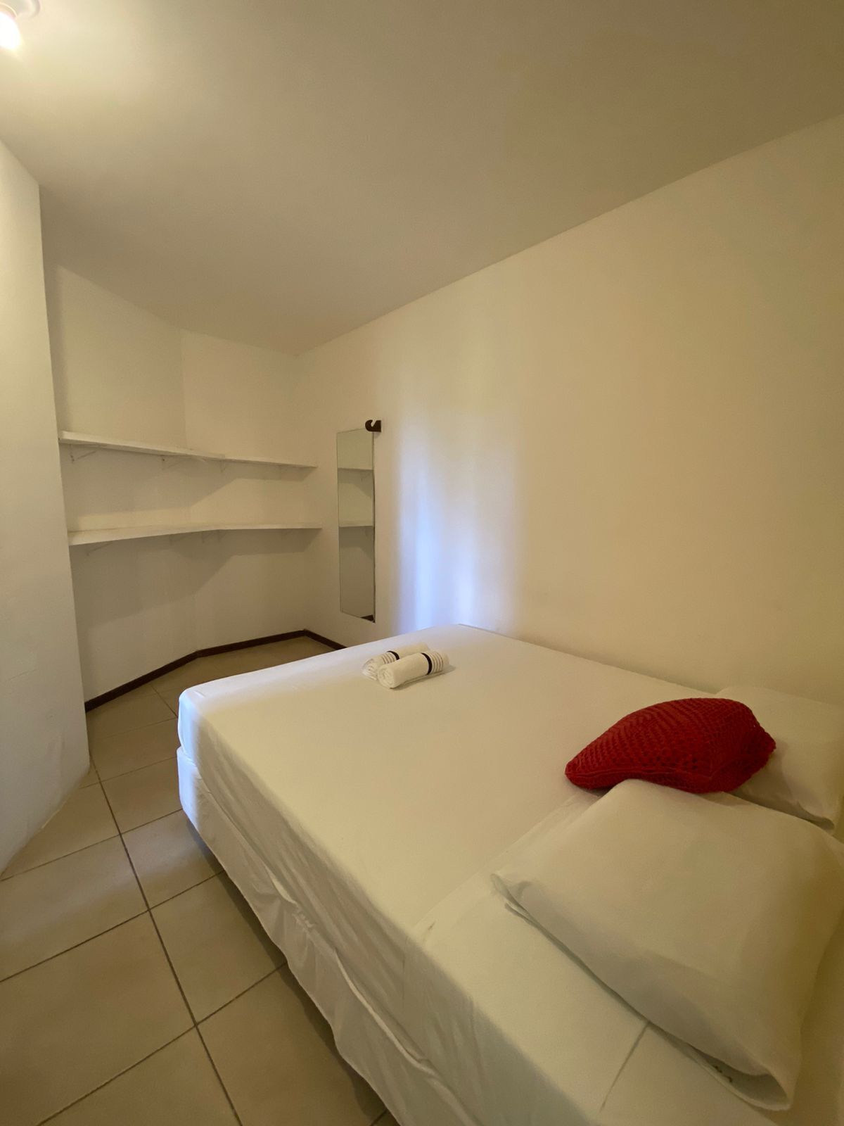 A hotel room with a single bed, white bedding, a red pillow, and a neatly folded towel.