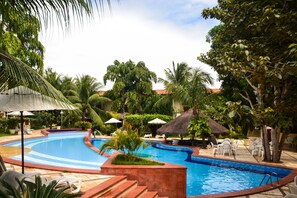 A swimming pool with a curved design, surrounded by palm trees and lounge chairs. - Solar da Gameleira (Tibau do Sul)