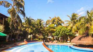 Una piscina con borde de baldosas, rodeada de palmeras y un cielo azul despejado.