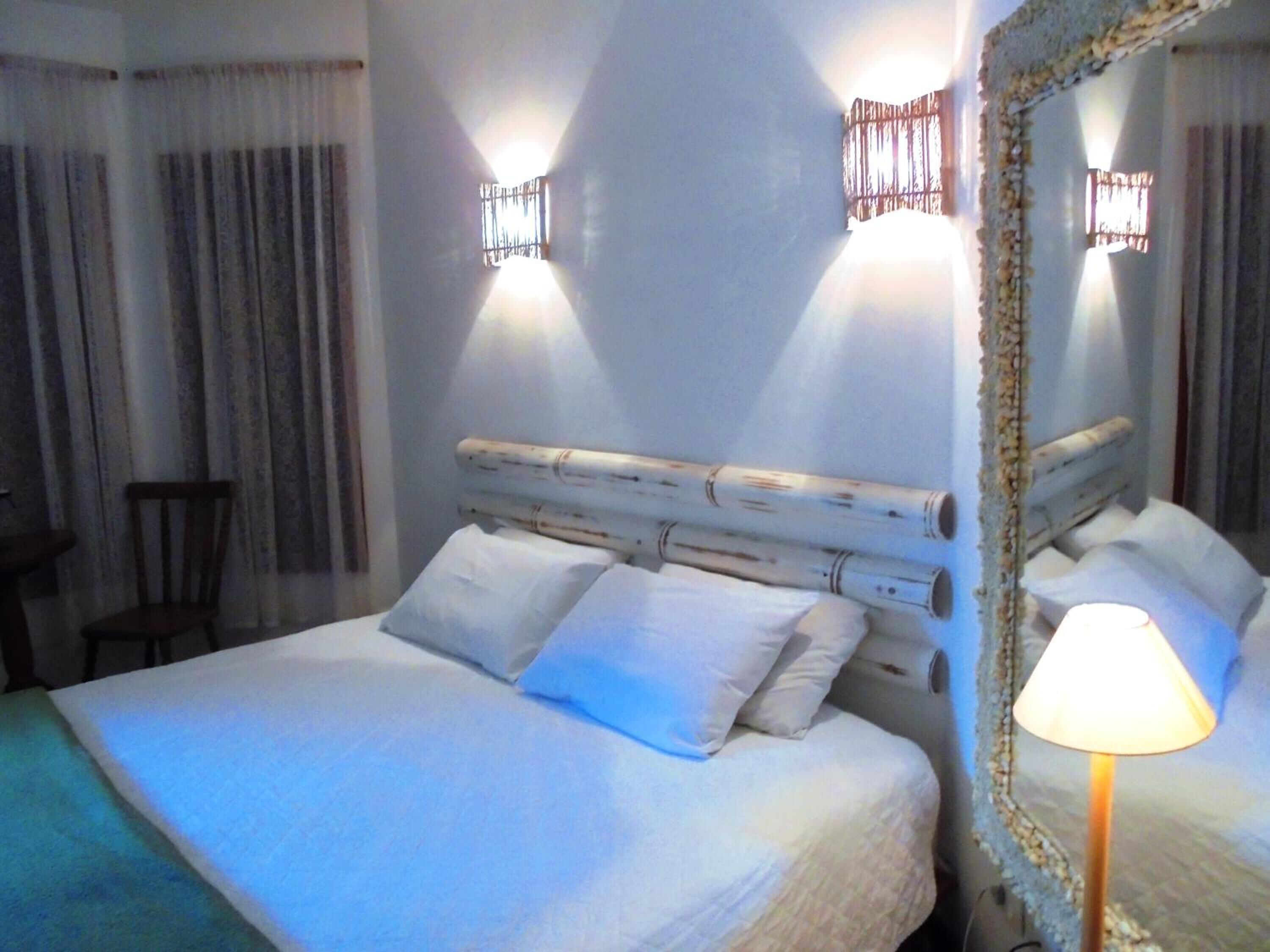 Una habitación de hotel con cama, una silla, una lámpara y un espejo.