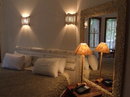 Un dormitorio con cama, dos lámparas de noche, teléfono y espejo con marco de piedra.