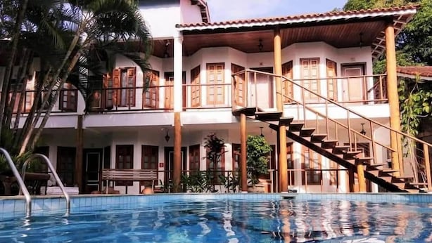 A two-story building with a swimming pool, wooden balconies, and a staircase leading to the upper level. - Pousada Náutilus (Ilhabela)
