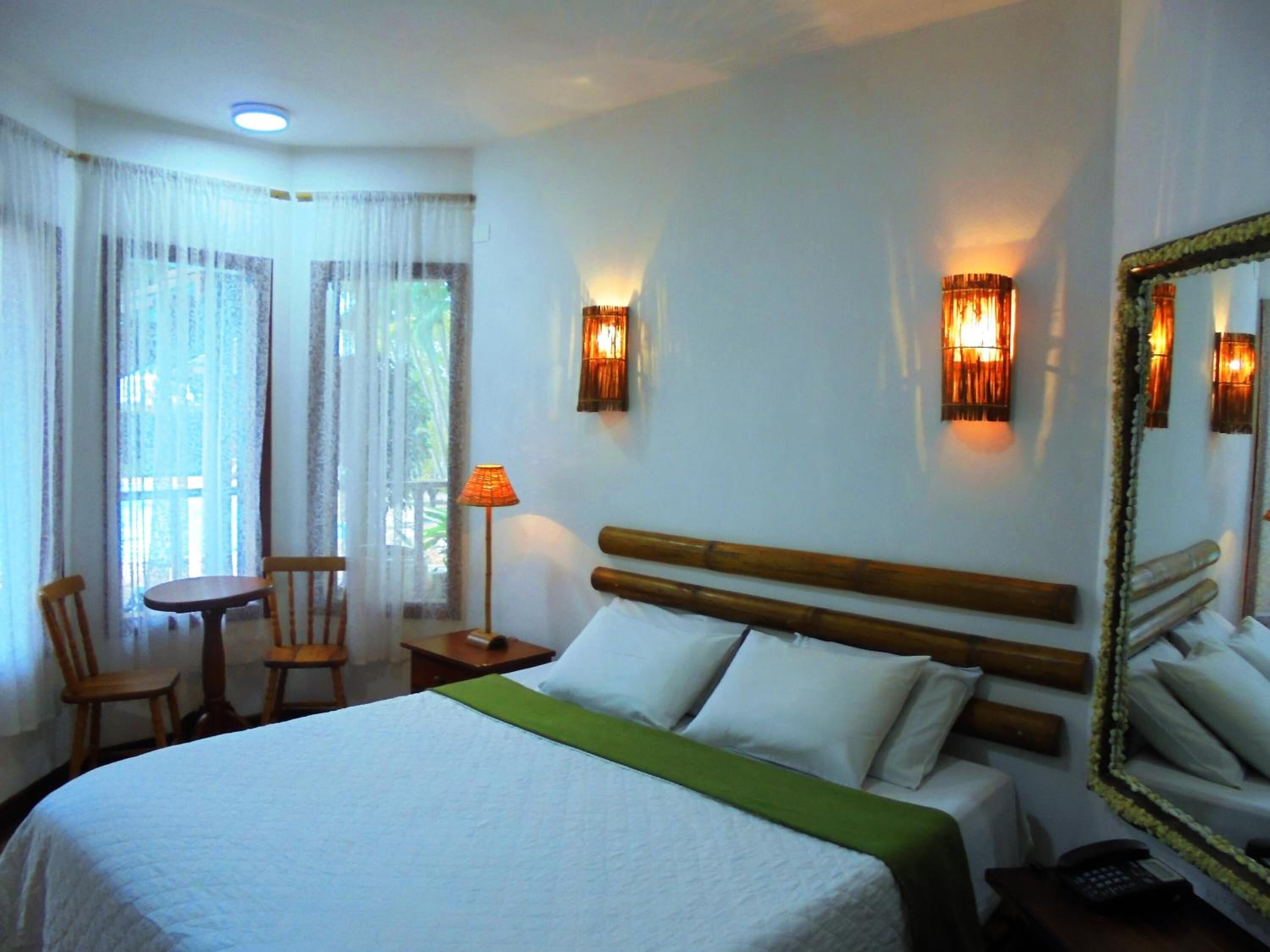 A hotel room with a bed, a table, two chairs, a lamp, and a mirror.
