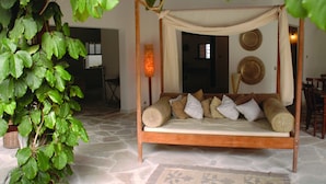 A four-poster bed with a canopy, surrounded by a stone floor, and a large green plant to the left. - Pousada Náutilus (Ilhabela)