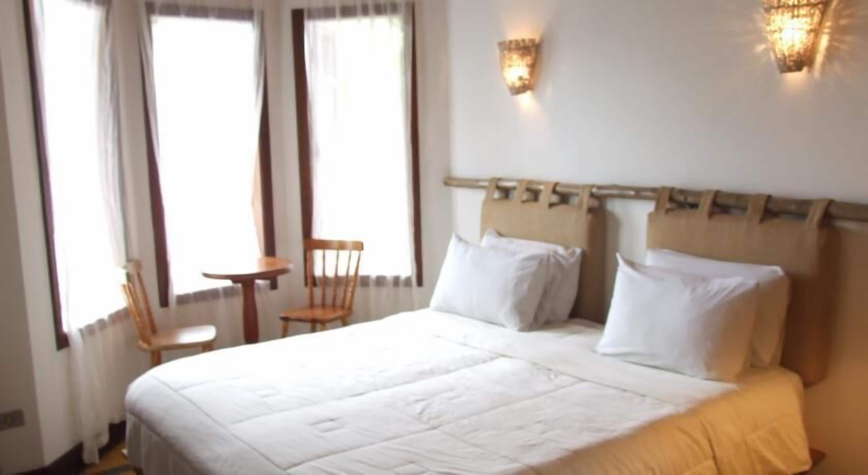 Ein Hotelzimmer mit einem großen Bett, zwei Nachttischen, einem Sessel und einem kleinen Tisch.