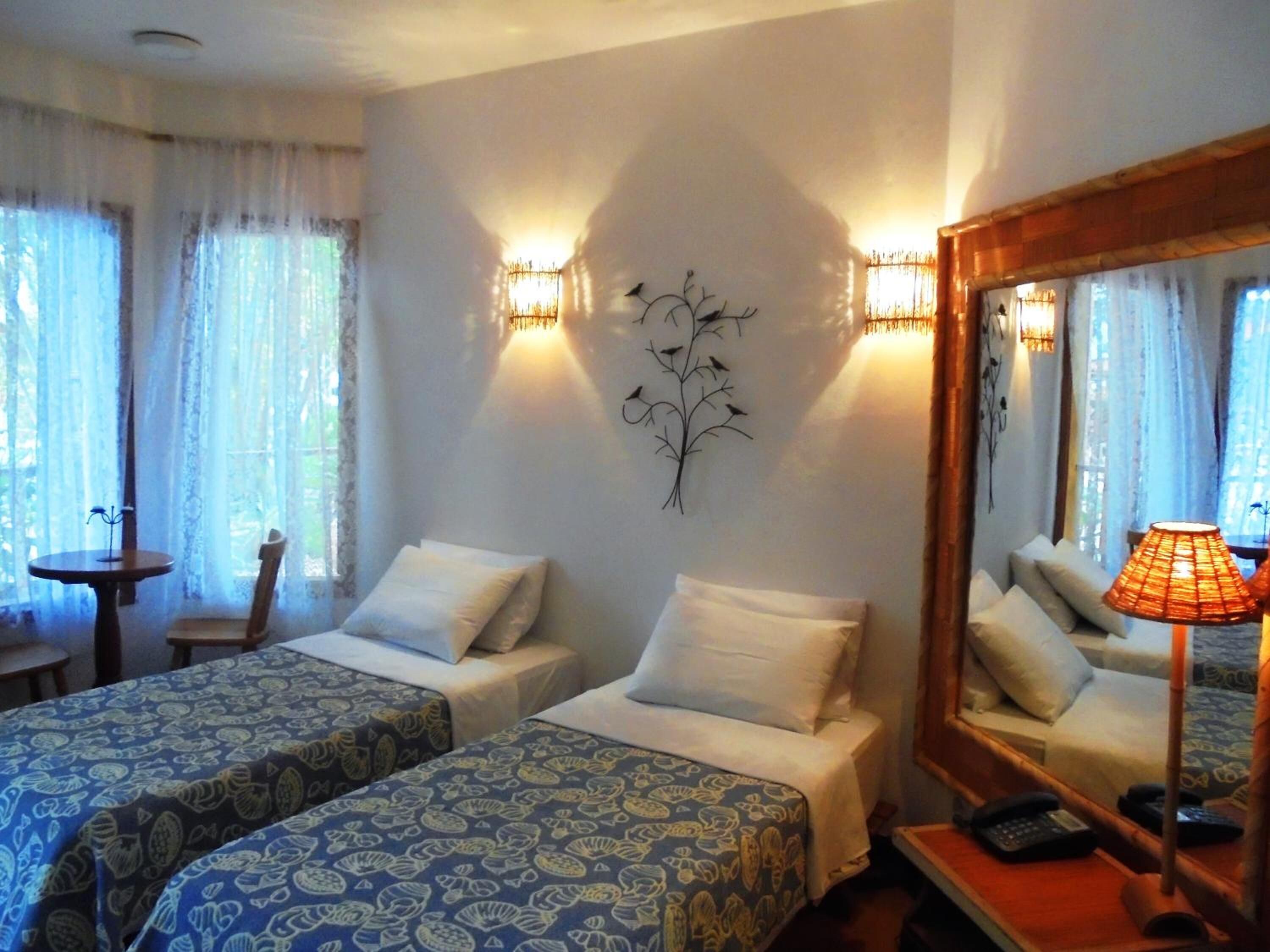 Une chambre d’hôtel avec deux lits, une petite table, une chaise, un miroir et une lampe fixée au mur.