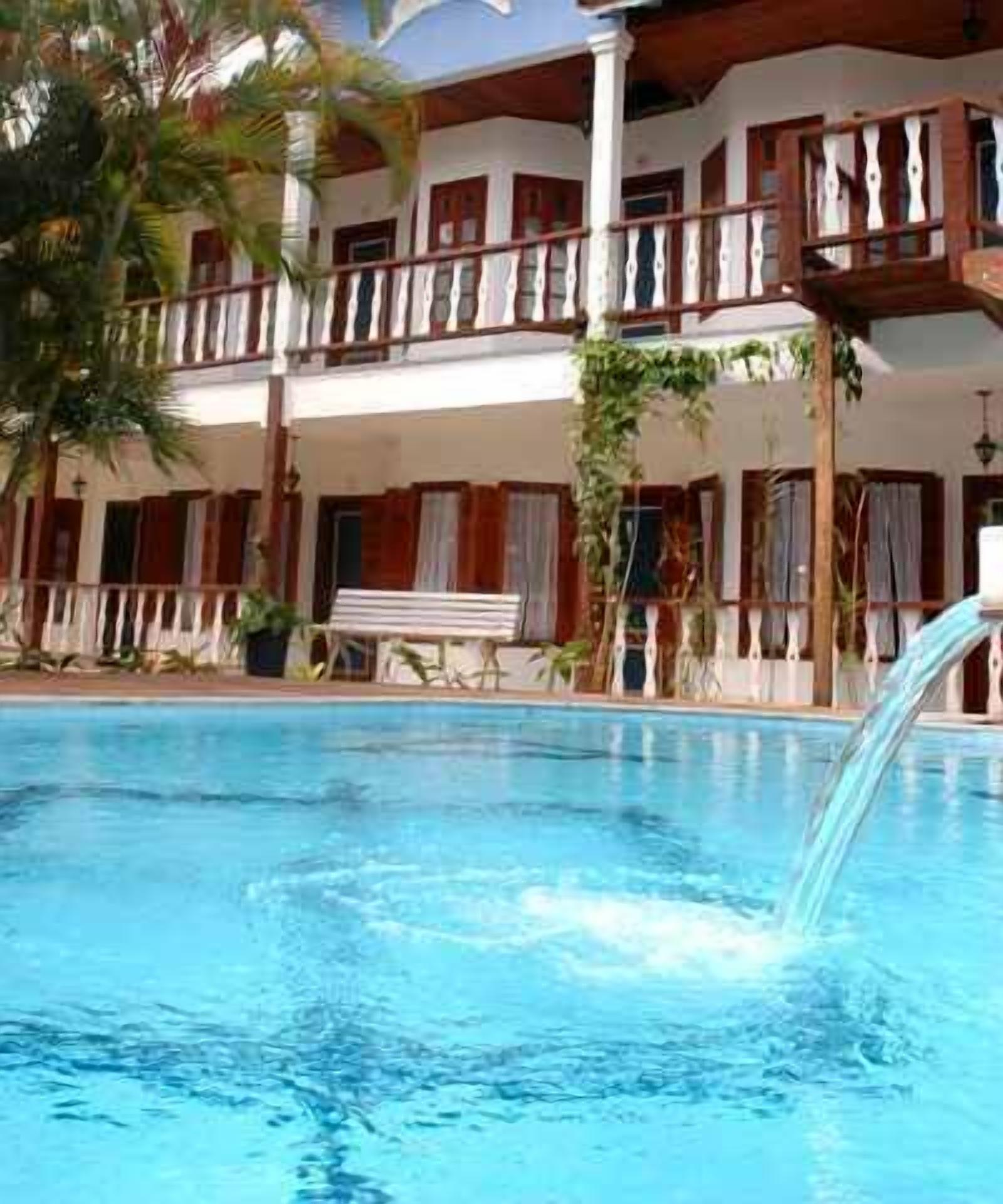 A swimming pool with a waterfall feature, surrounded by a two-story building with balconies and wooden railings.