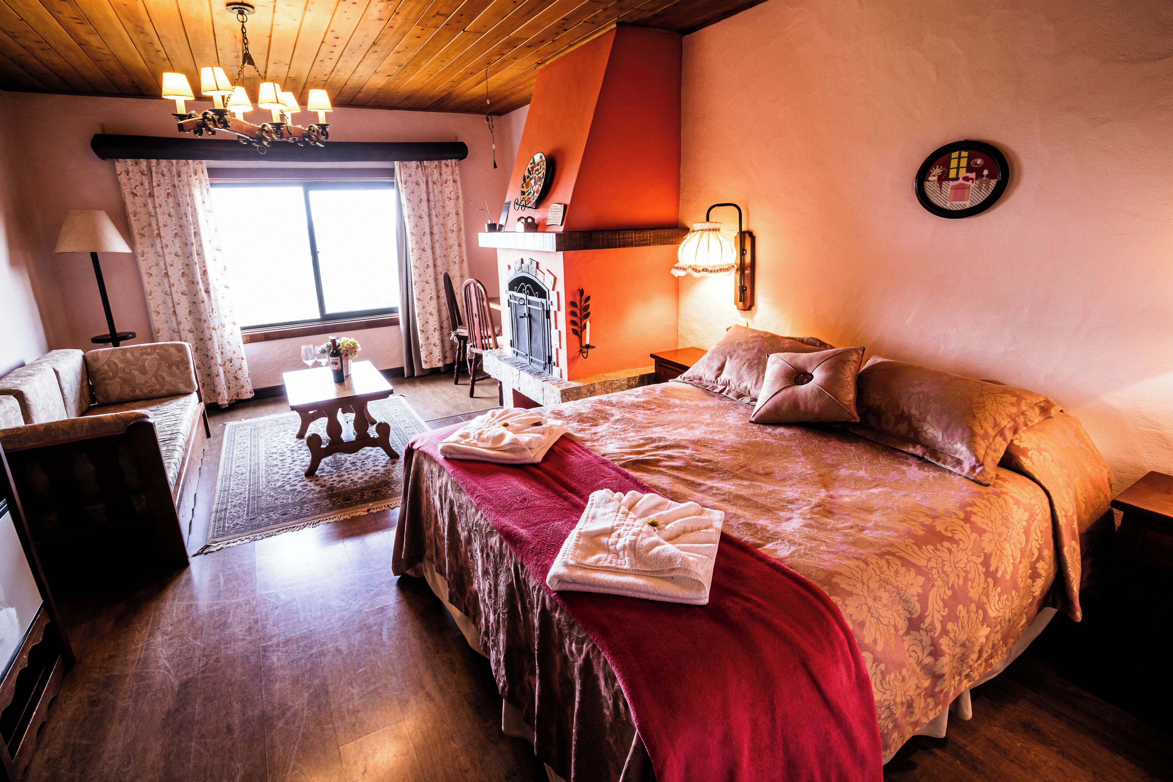 Una habitación de hotel acogedora con una cama grande, chimenea, comedor y vistas al exterior.