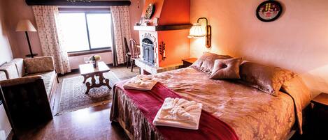 Una habitación de hotel acogedora con una cama grande, chimenea, comedor y vistas al exterior.