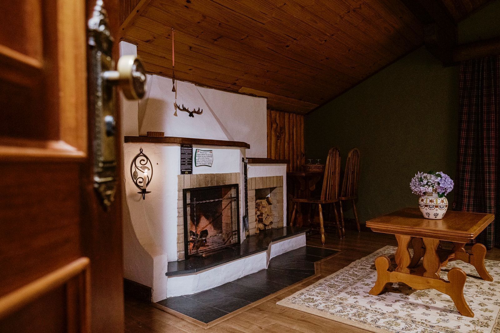 Une pièce chaleureuse avec une cheminée, un plafond en bois et une table à manger avec des chaises.