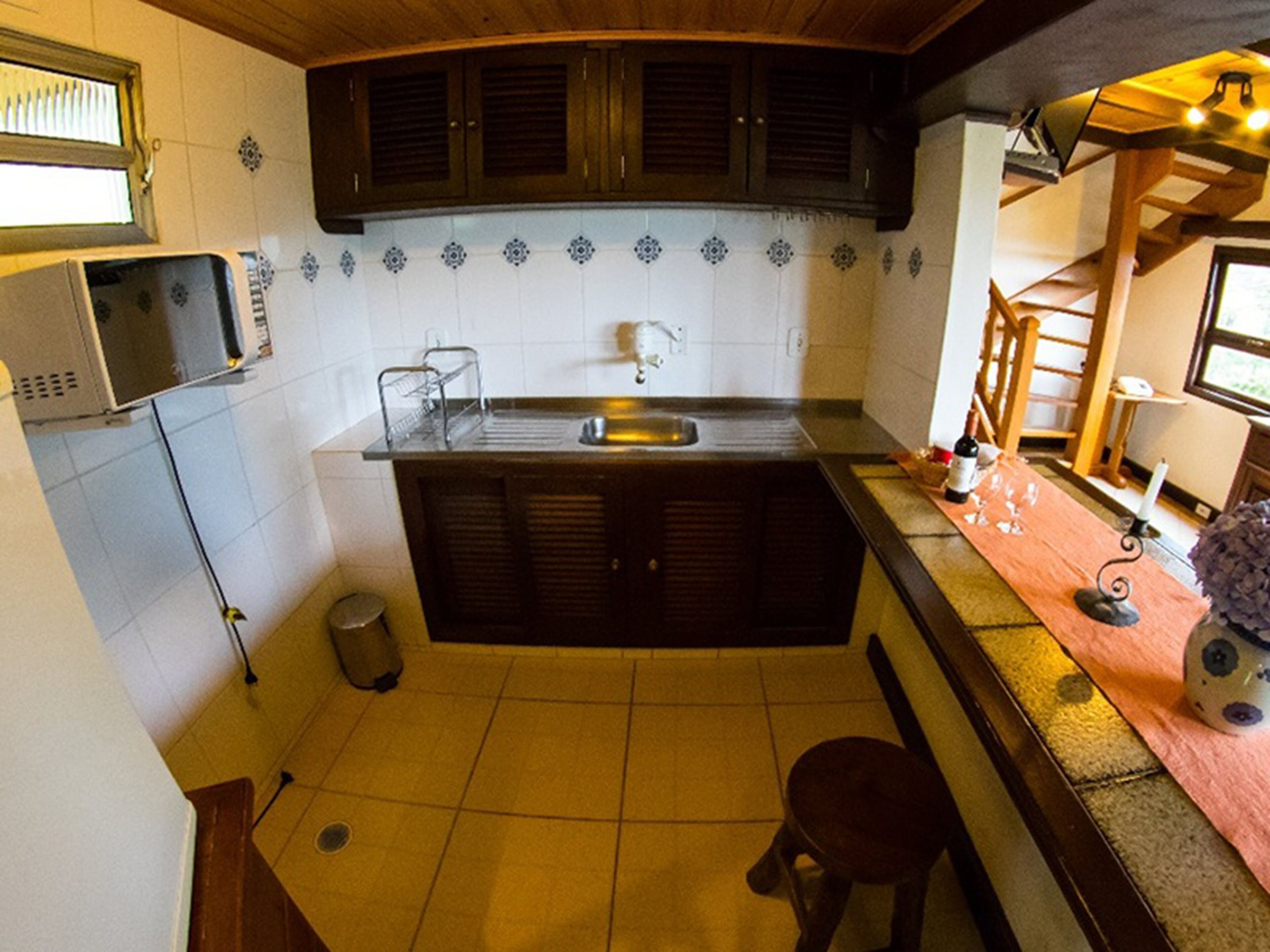 Cocina compacta con un lavamanos, microondas y un taburete pequeño.