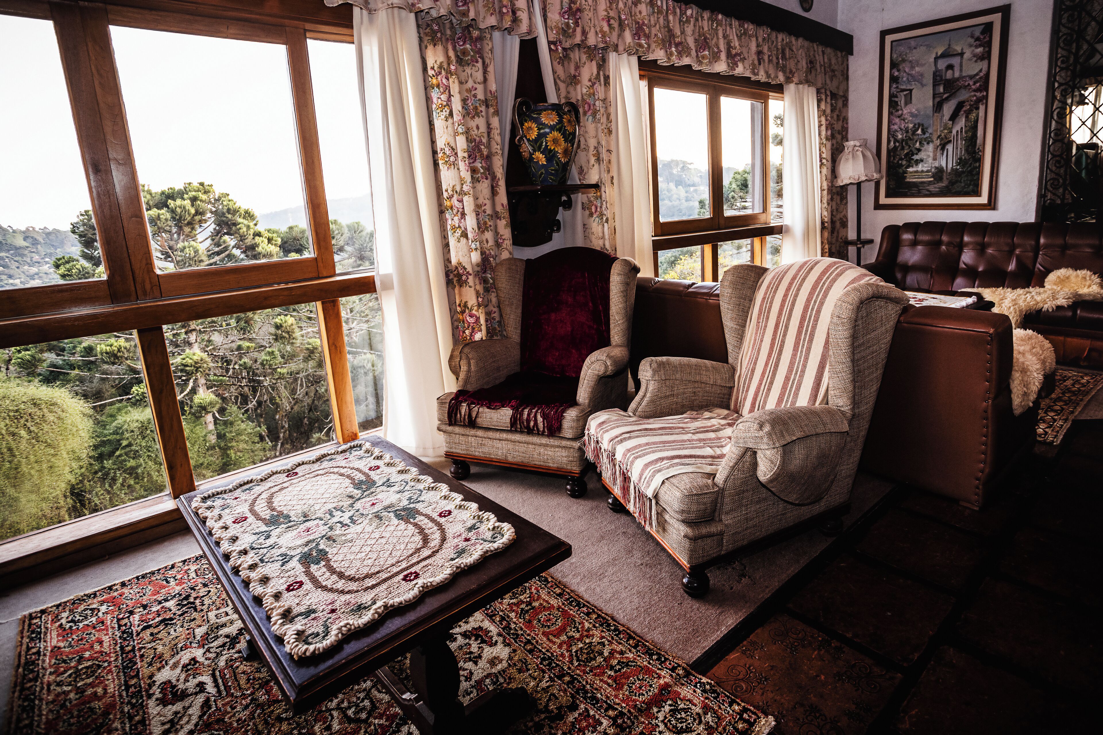 A cozy room with a large window, a patterned rug, a cushioned chair, and a framed picture on the wall.