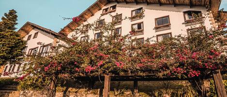 A traditional building with multiple balconies, a stone wall, and a wooden pergola with a hanging chair.