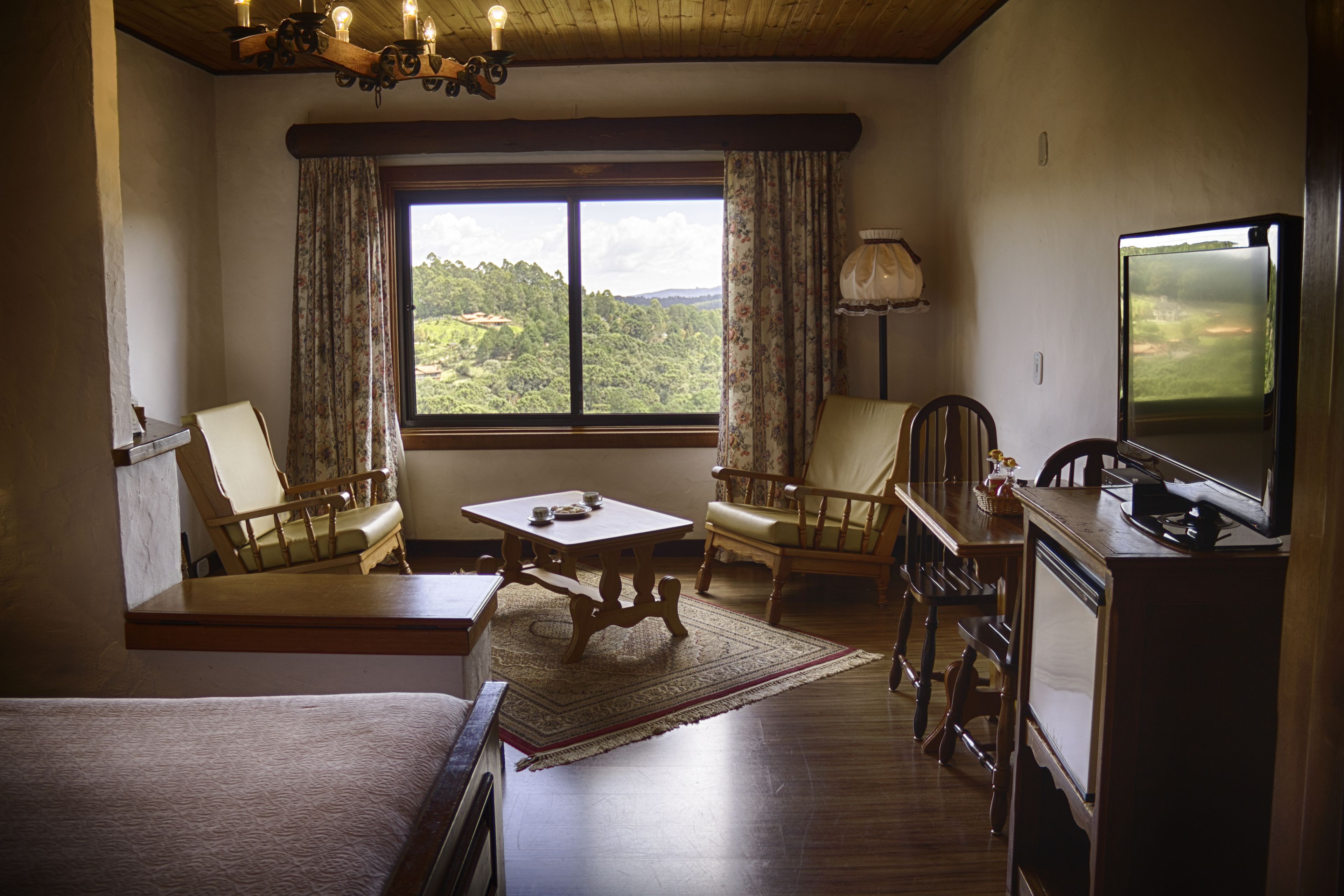 Una habitación con techo de madera, un ventanal con cortinas, un televisor, una mesa de madera y dos sillas.