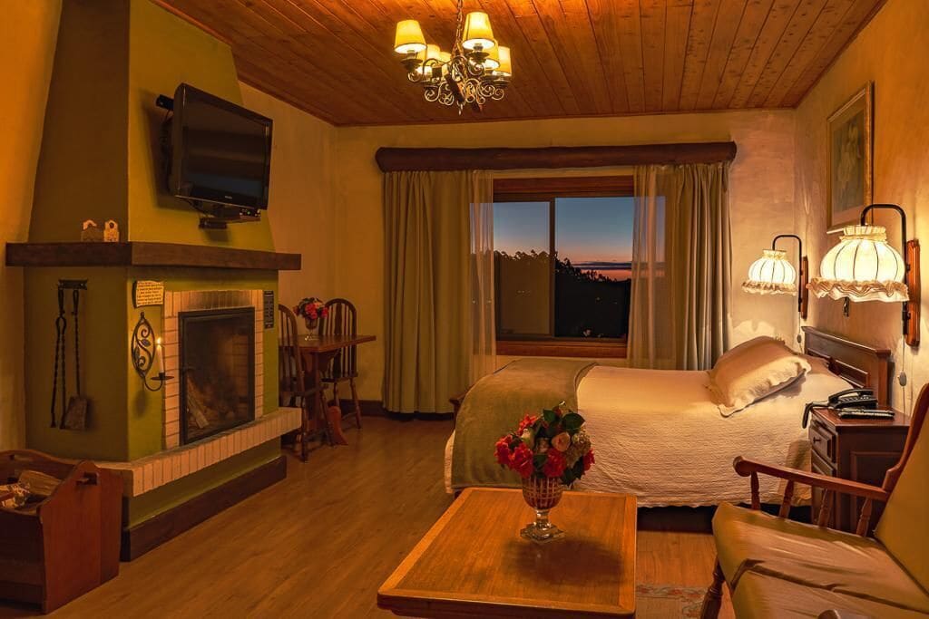 A cozy room with a fireplace, a bed, a television, and a large window with a view.