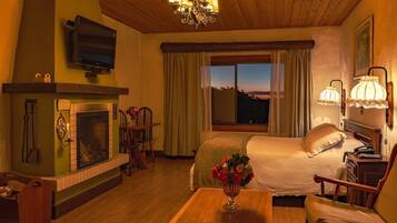 A cozy room with a fireplace, a bed, a television, and a large window with a view.