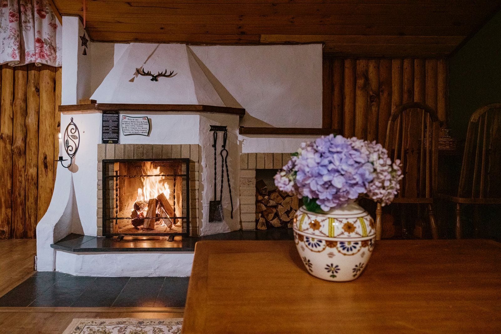 Una habitación acogedora con chimenea, una mesa de madera y un jarrón decorativo.