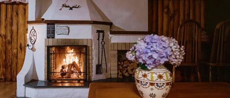 Una habitación acogedora con chimenea, una mesa de madera y un jarrón decorativo.