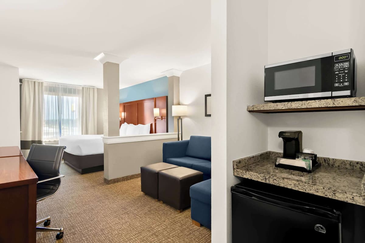 A hotel room with a bed, a desk, a chair, a sofa, a microwave, a coffee maker, and a small refrigerator.