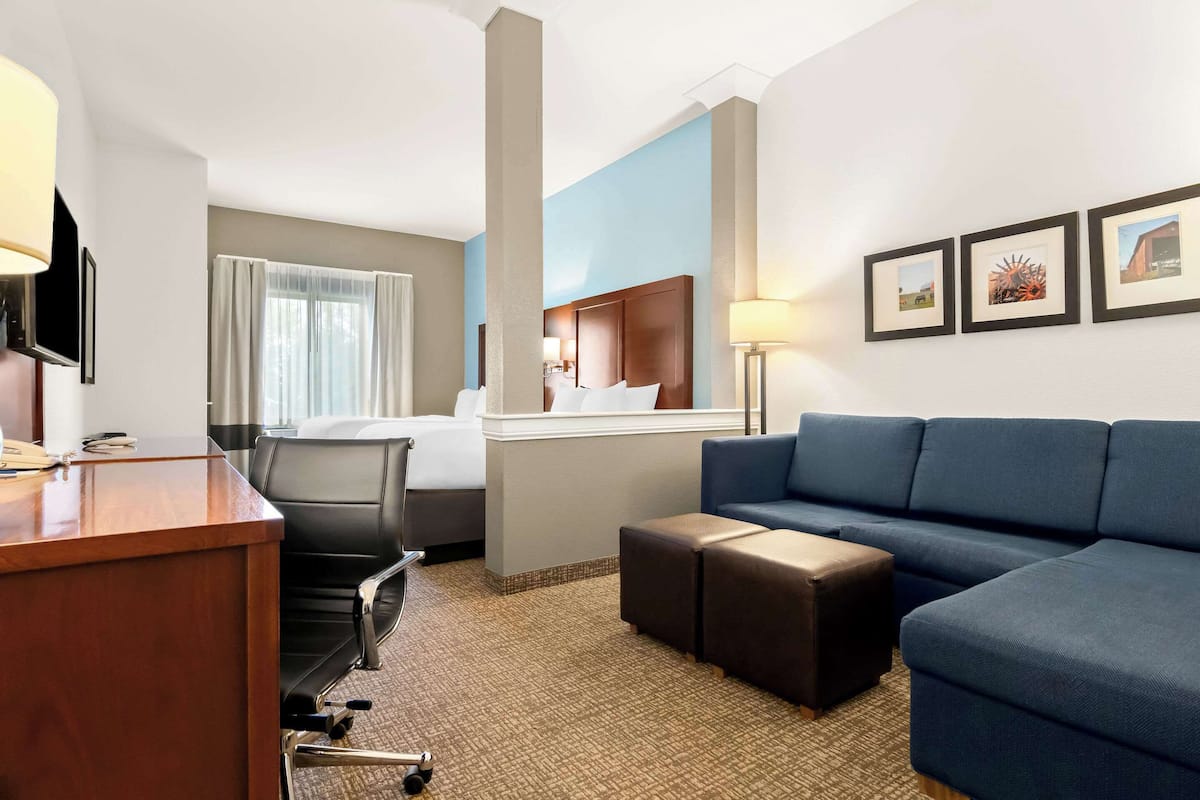 A hotel room with a desk, a bed, a blue sofa, and a small table.