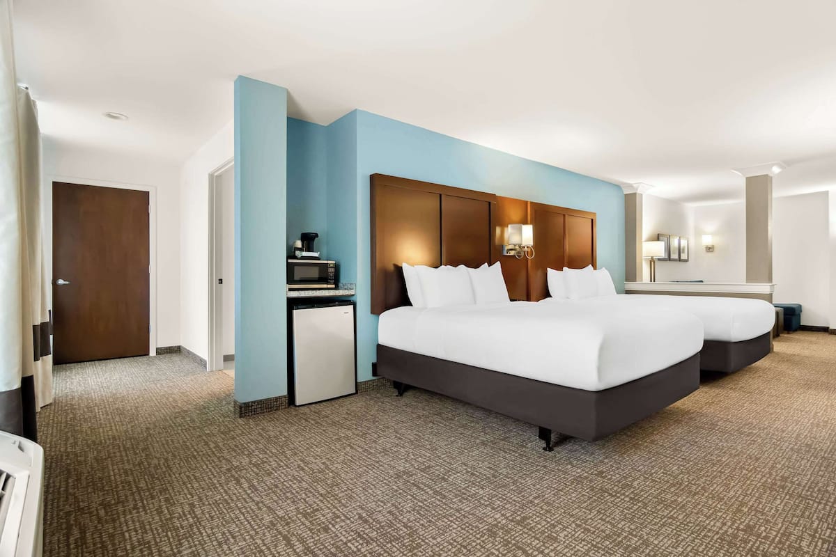 A hotel room with a large bed, a desk with a coffee maker, and a small refrigerator.