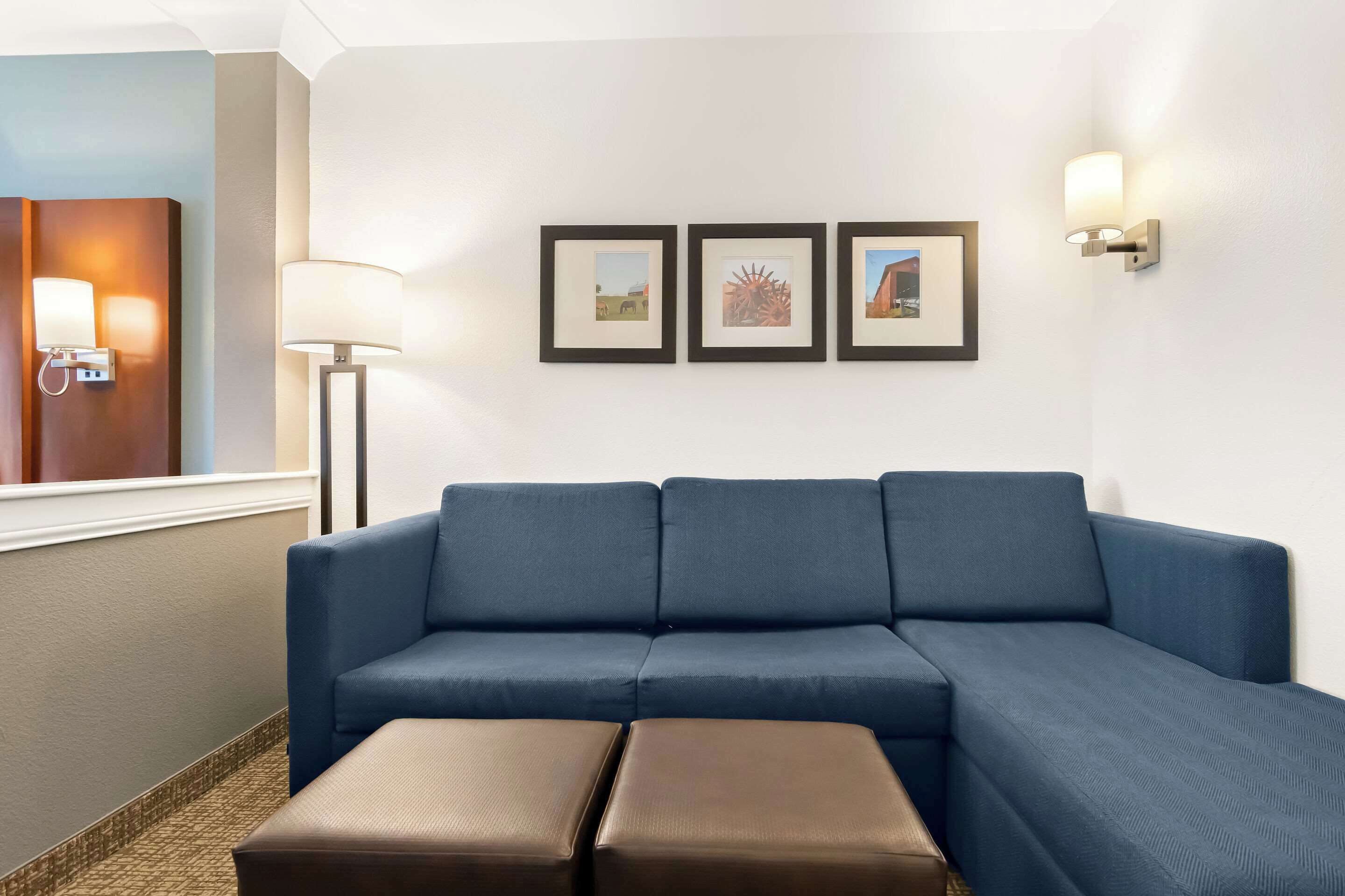 A modern living room with a blue sectional sofa, two brown ottomans, a floor lamp, and three framed pictures on the wall.