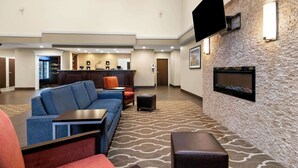 A spacious lobby with a modern design, featuring a large seating area with sofas and armchairs, a flat-screen TV mounted on the wall, and a fireplace. - Comfort Suites Rensselaer near Fair Oaks (Rensselaer)