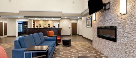 A spacious lobby with a modern design, featuring a large seating area with sofas and armchairs, a flat-screen TV mounted on the wall, and a fireplace.