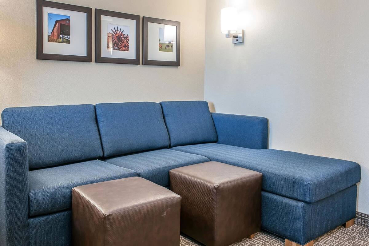 A sectional sofa with two ottomans, framed pictures on the wall, and a wall-mounted light fixture.