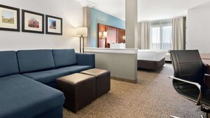 A hotel room with a blue sofa, a bed, a desk, a chair, and framed pictures on the wall. - Comfort Suites Rensselaer near Fair Oaks (Rensselaer)
