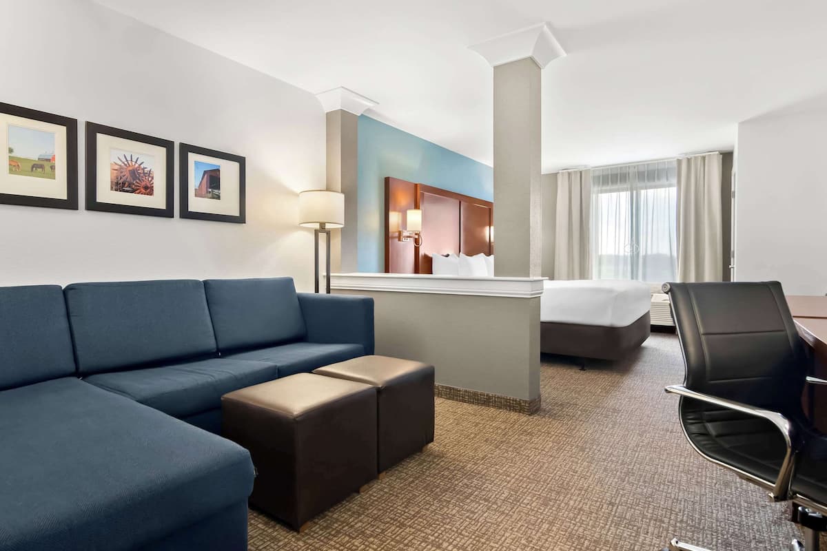 A hotel room with a blue sofa, a bed, a desk, a chair, and framed pictures on the wall.