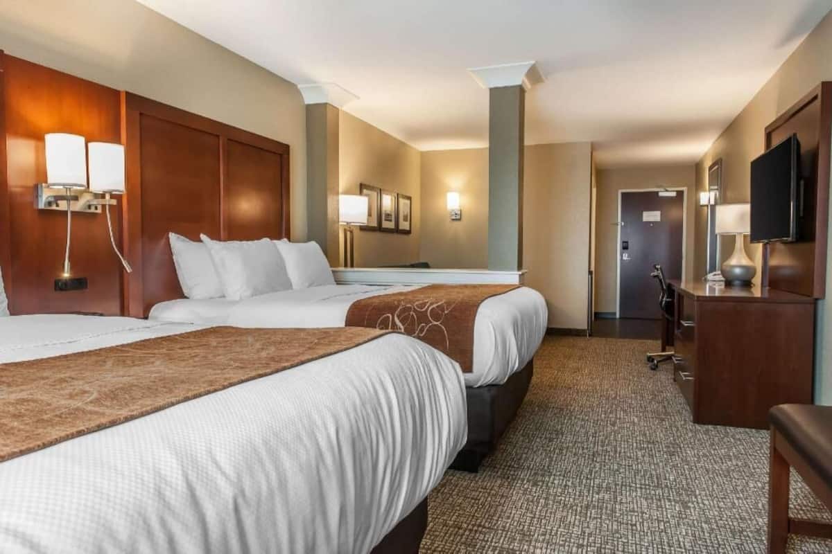 A hotel room with two beds, a desk, a TV, and a lamp.