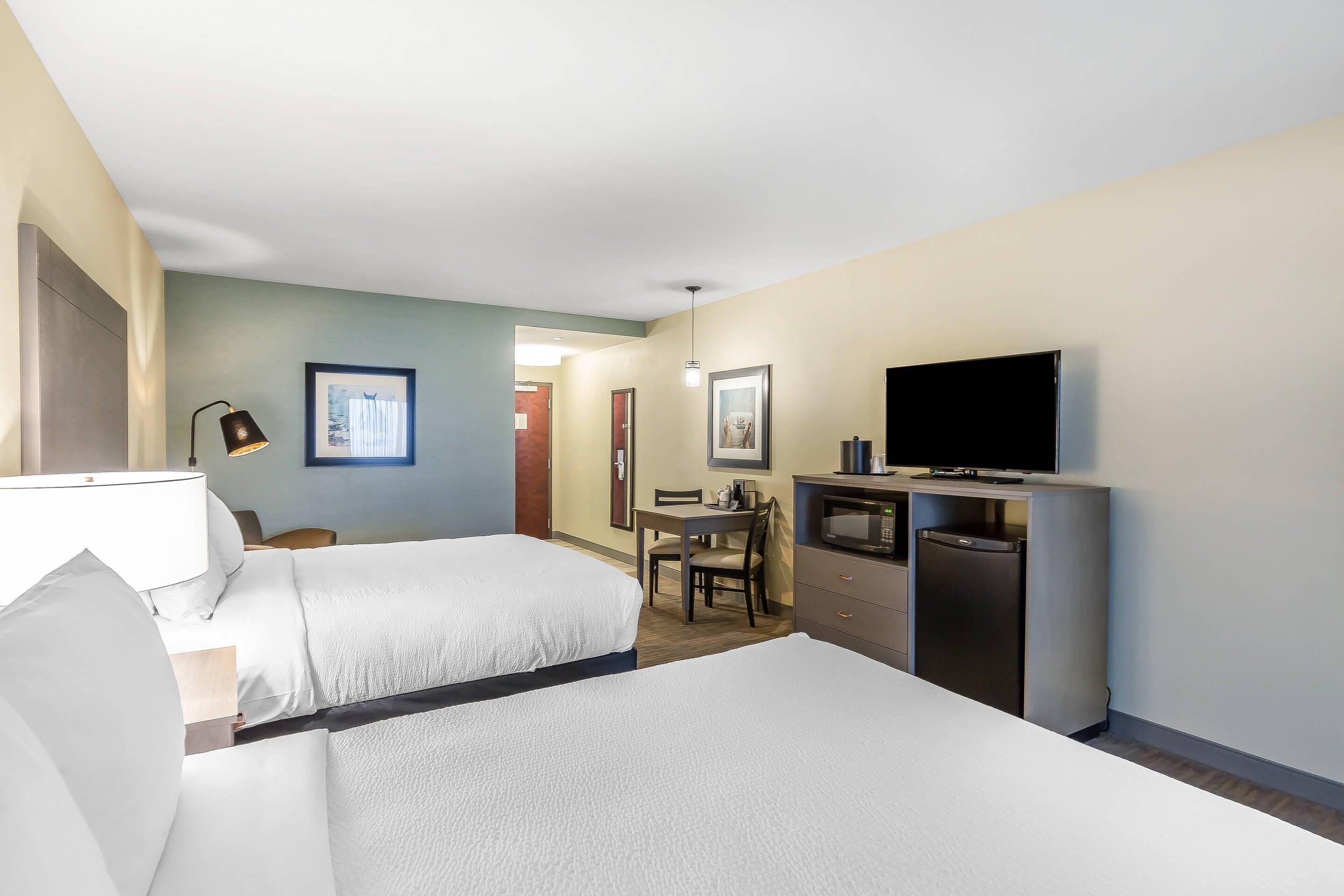 A hotel room with two beds, a desk, a television, and a minibar.