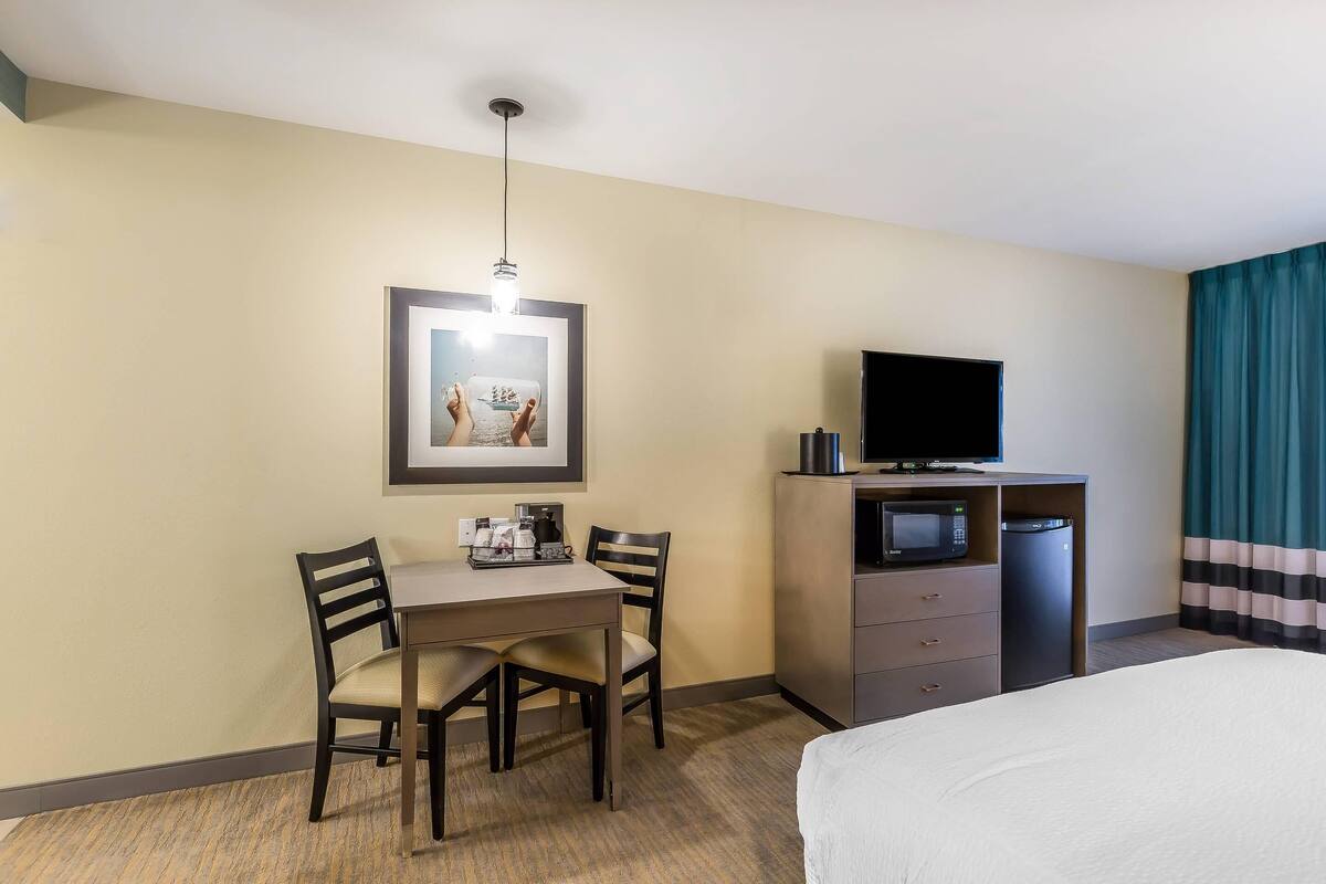 Une chambre d’hôtel équipée d’un lit, d’un bureau avec une chaise, d’une télévision, d’un four à micro-ondes et d’une machine à café.