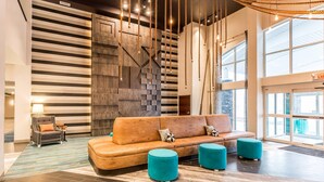 Een moderne lobby met een houten bank, smaragdgroene poefs en een gestreepte wand.