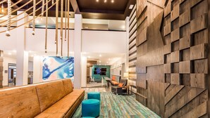 Een moderne lobby met een houten bank, blauwe poefs en een kleurrijk abstract schilderij.