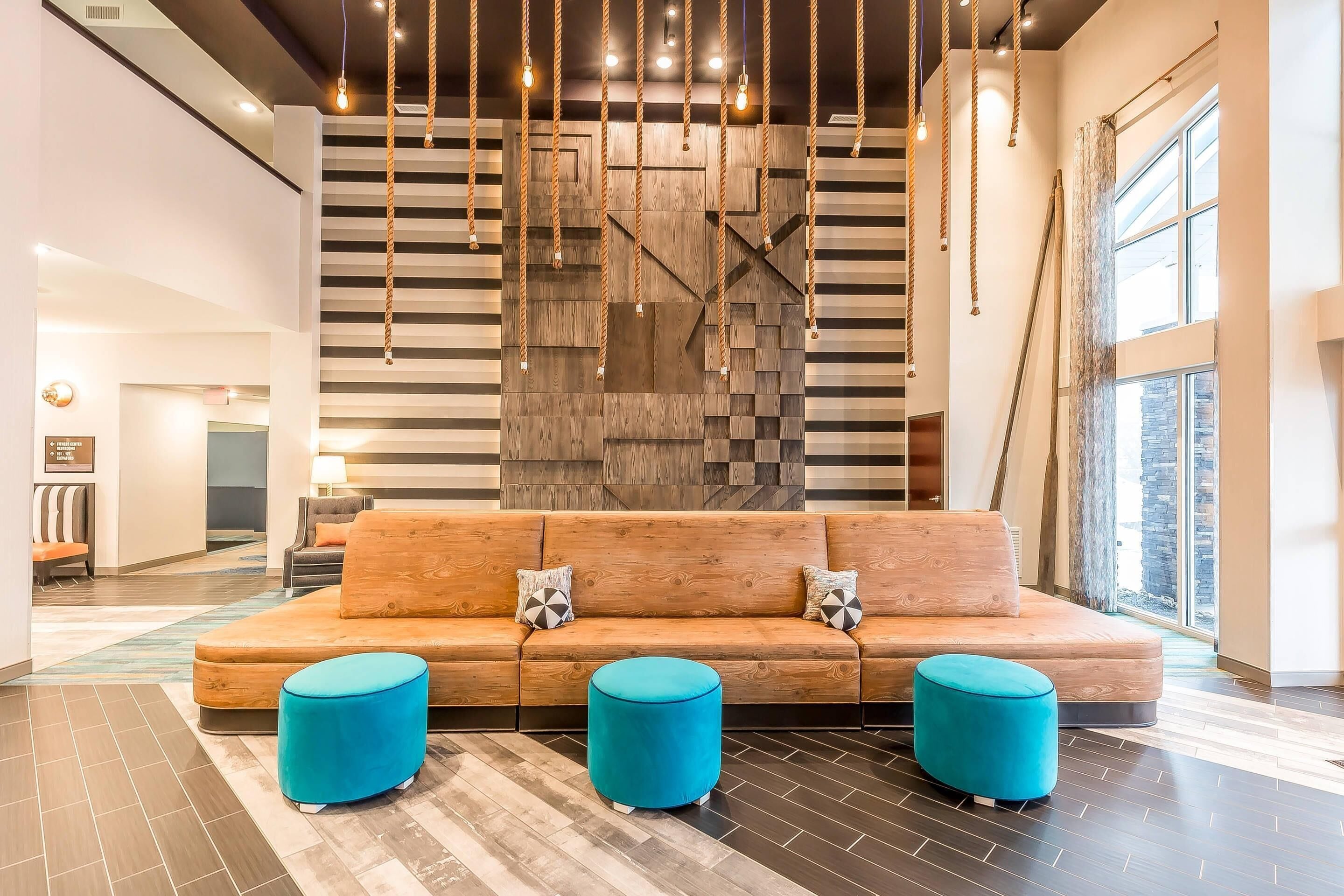 A modern lobby with a wooden accent wall, a sofa with cushions, and two round ottomans.
