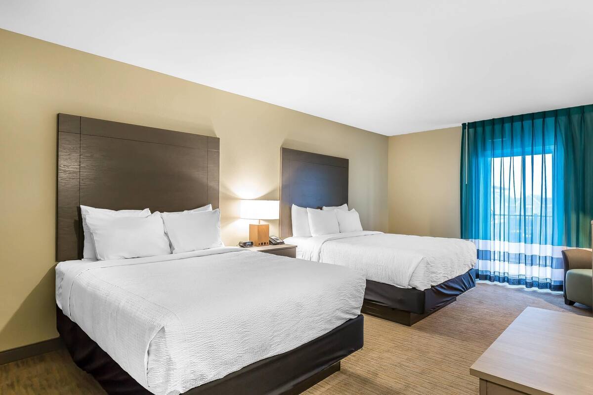 Une chambre d’hôtel avec deux lits, un bureau, une chaise et une fenêtre avec des rideaux.