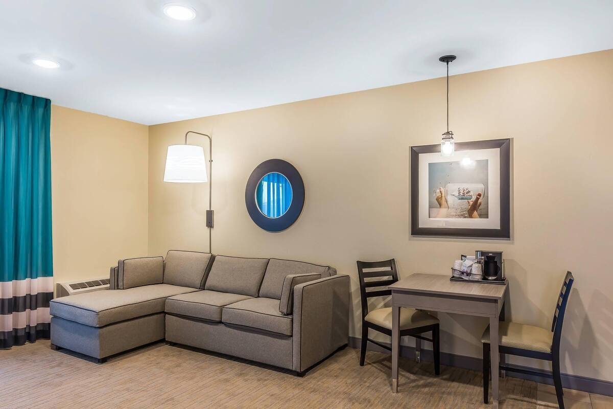 Une chambre d’hôtel moderne, dotée d’un canapé d’angle, d’une table à manger avec des chaises, d’une lampe fixée au mur et d’un tableau encadré.